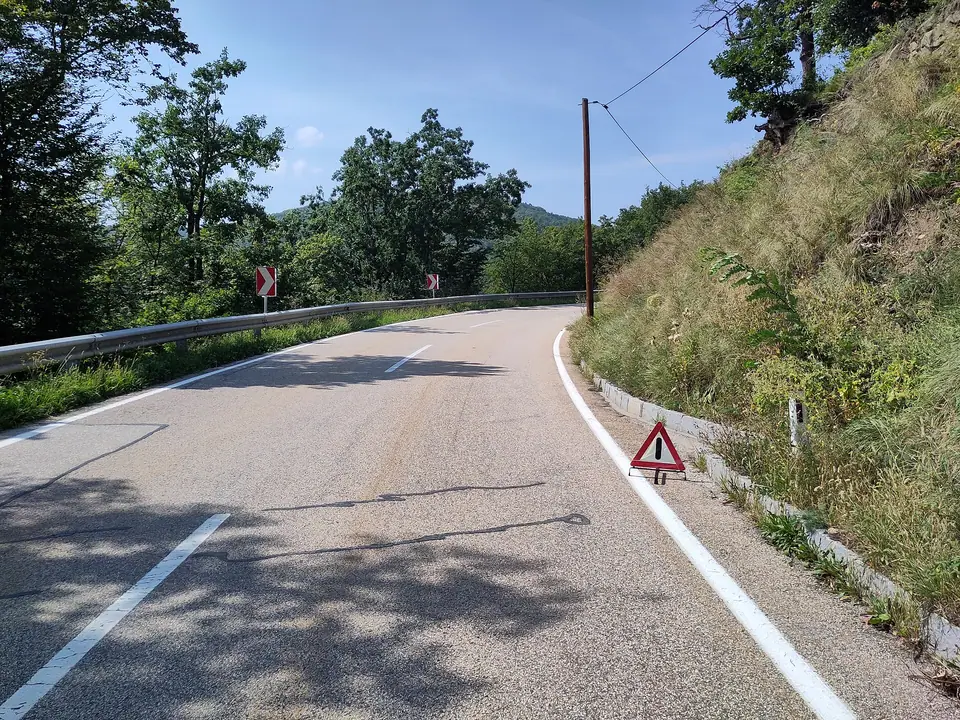 Virajlı bir yolun sağ kenarına, beyaz kenar çizgisinin yanına konmuş kırmızı reflektörlü yol üçgeni
